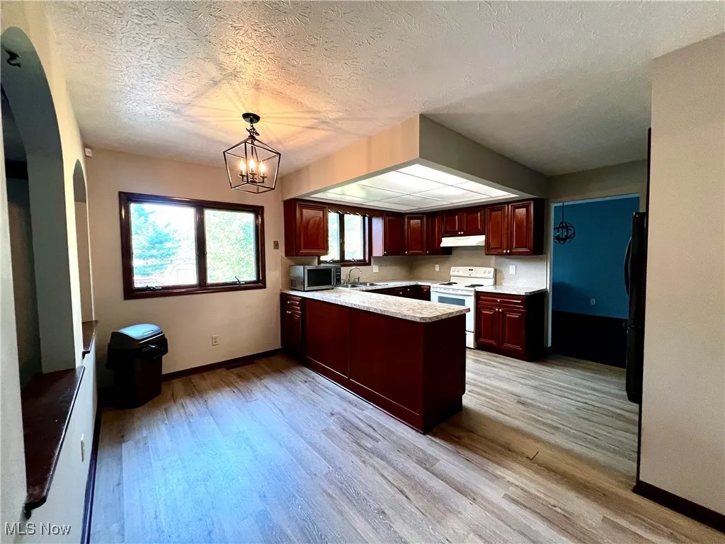 Eat in kitchen featuring a peninsula, white electric range oven, light wood-type flooring, dark brown cabinets, and a textured ceiling