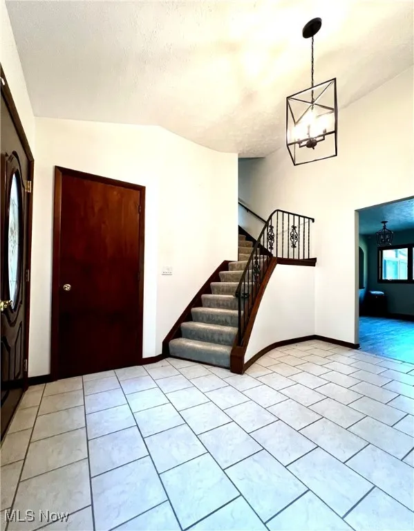 Foyer with lofted ceiling, a chandelier, stairs, light tile patterned flooring, and a textured ceiling