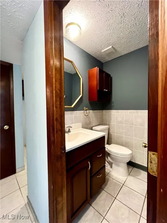 First floor half bath with a textured ceiling, tile patterned floors, vanity and tile walls