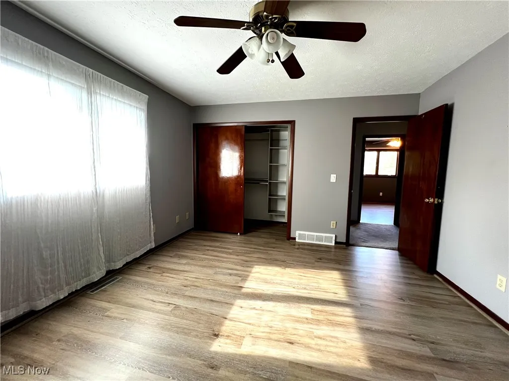 Unfurnished primary bedroom with luxury vinyl floors, a textured ceiling, ceiling fan, and a closet system