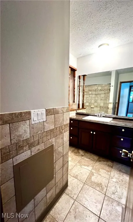 Second floor full-bathroom with vanity, tile patterned floors, a textured ceiling and tile walls