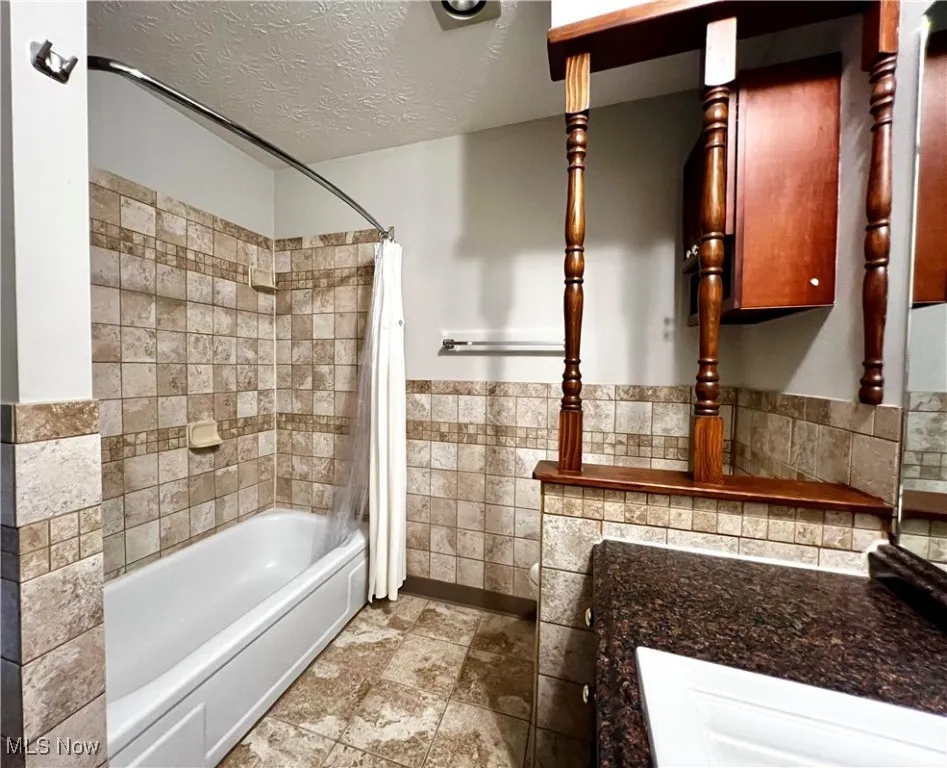 Second floor full-bathroom featuring shower / bath combination with curtain, tile walls and textured ceiling,