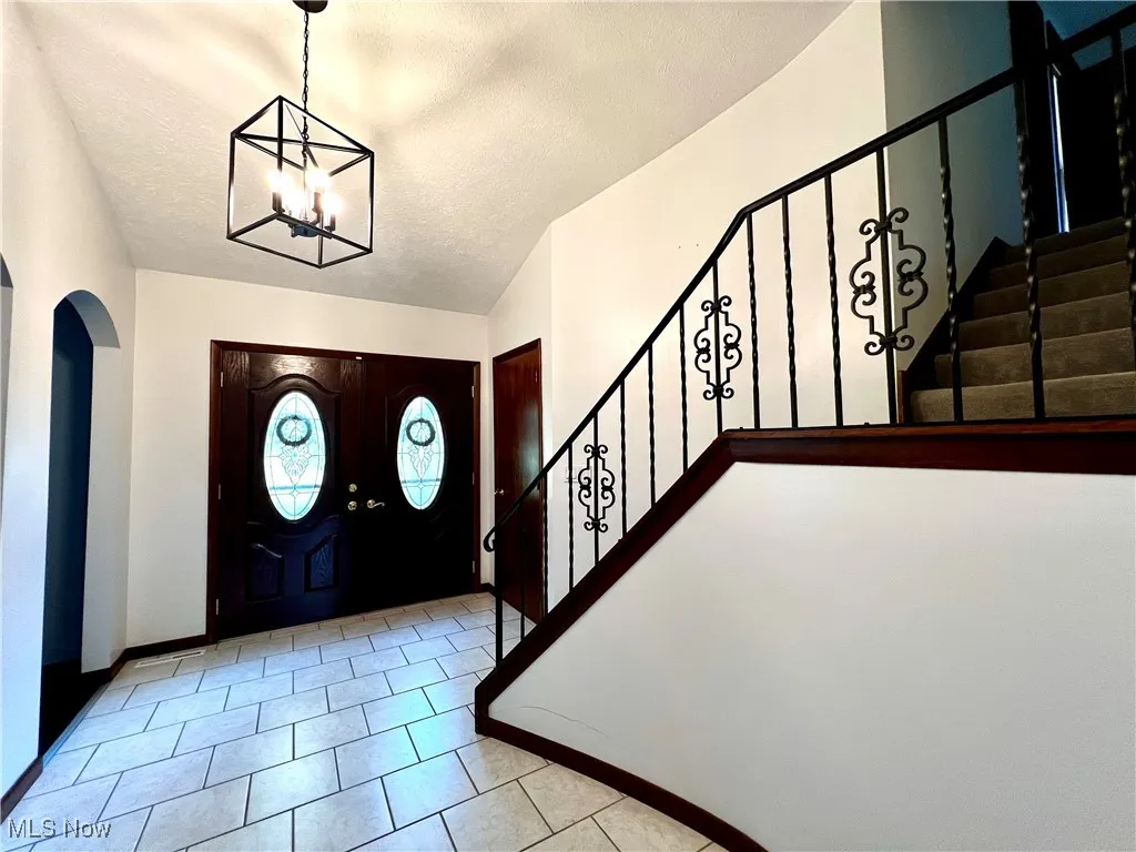 Tiled foyer entrance with stairs, arched walkways, a textured ceiling, and a chandelier