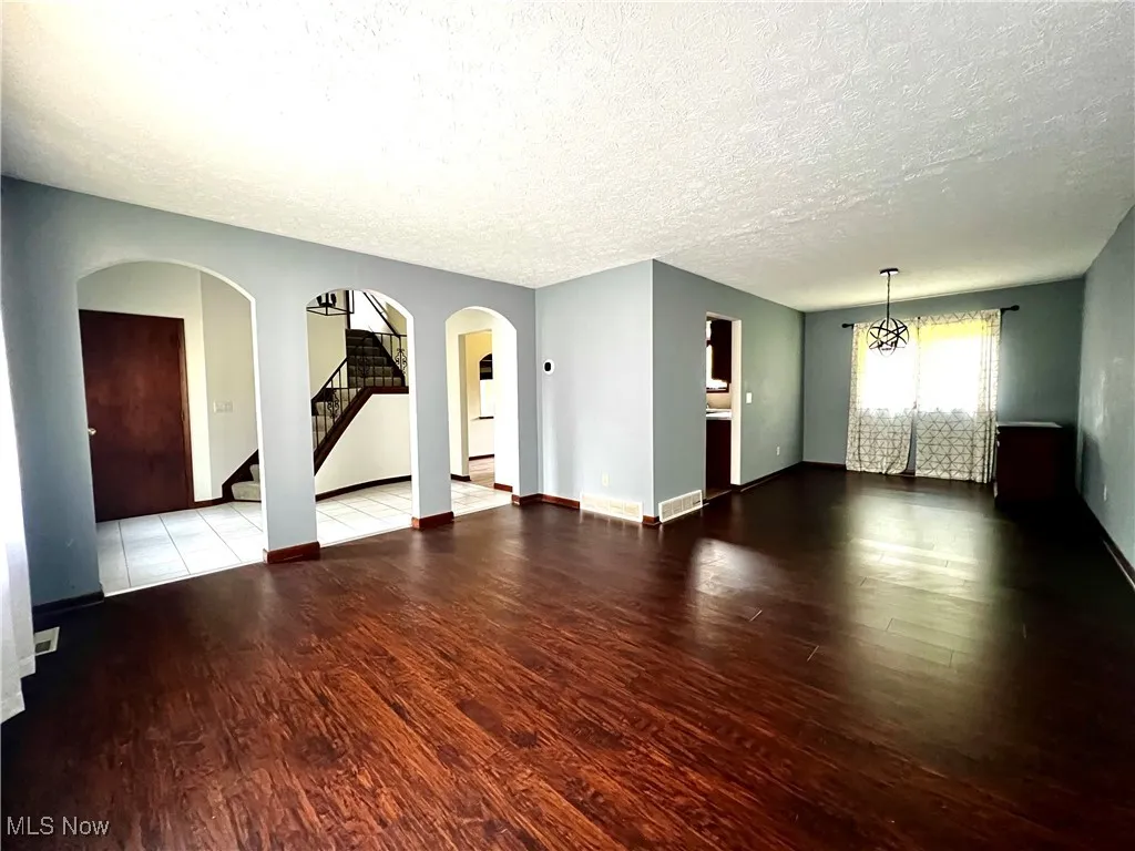 Unfurnished living room featuring stairs, wood finished floors, a textured ceiling, and arched walkways