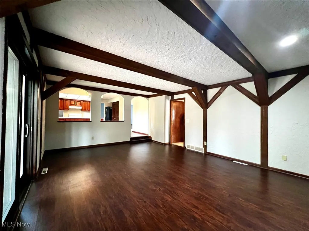 Additional living space with beamed ceiling, arched walkways, a textured ceiling, and dark wood-style floors