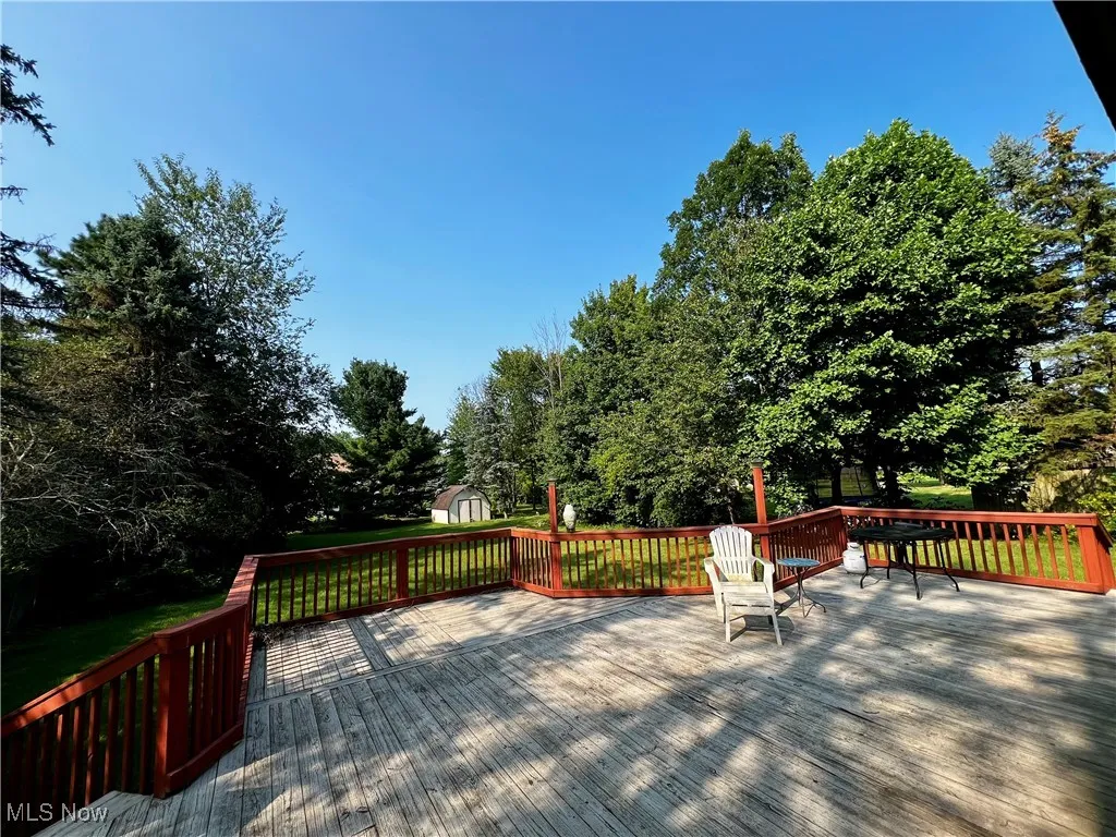Wooden terrace with a shed, view of scattered trees, and a yard