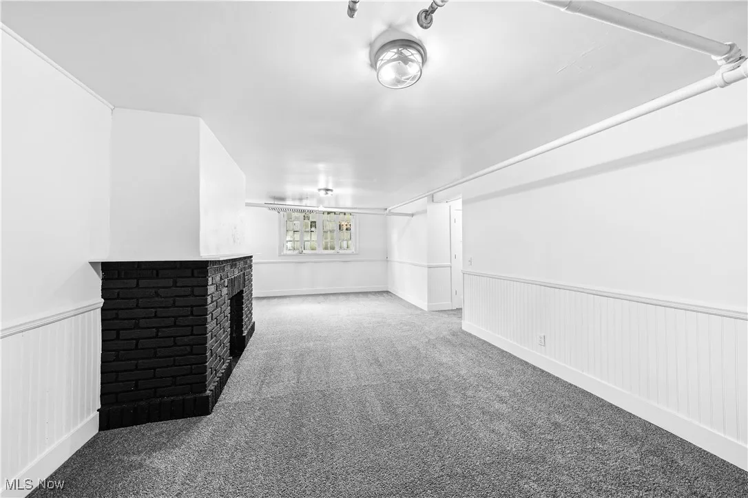 Unfurnished living room featuring wainscoting, a brick fireplace, and carpet floors