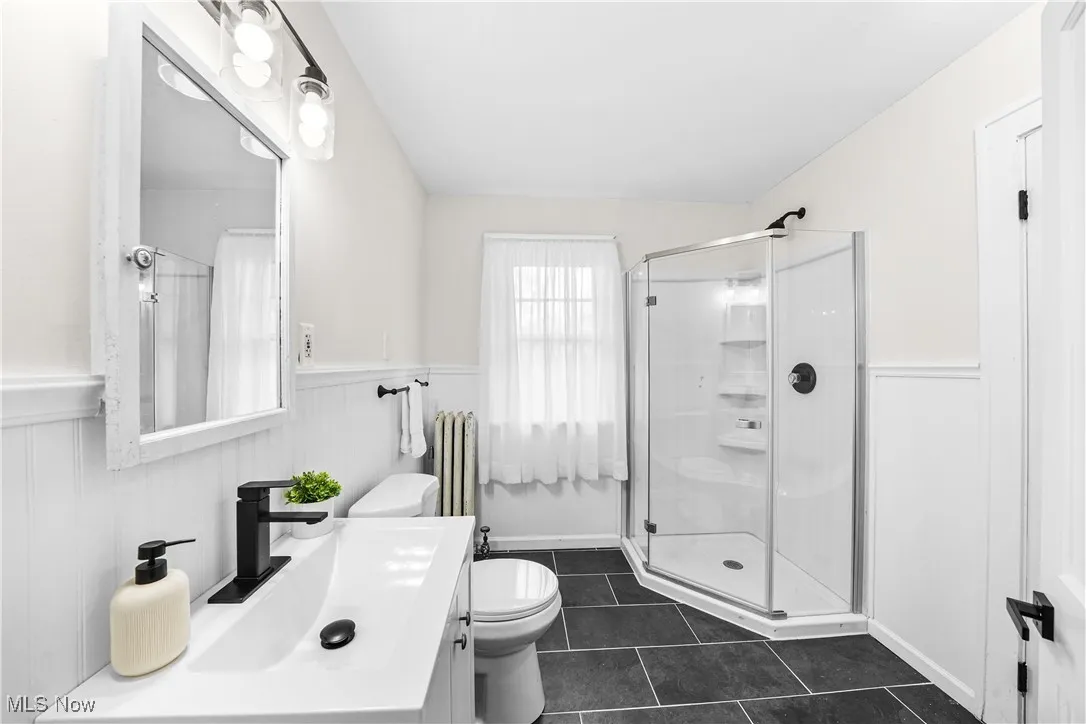 Bathroom featuring wainscoting, a stall shower, vanity, tile patterned flooring, and a decorative wall