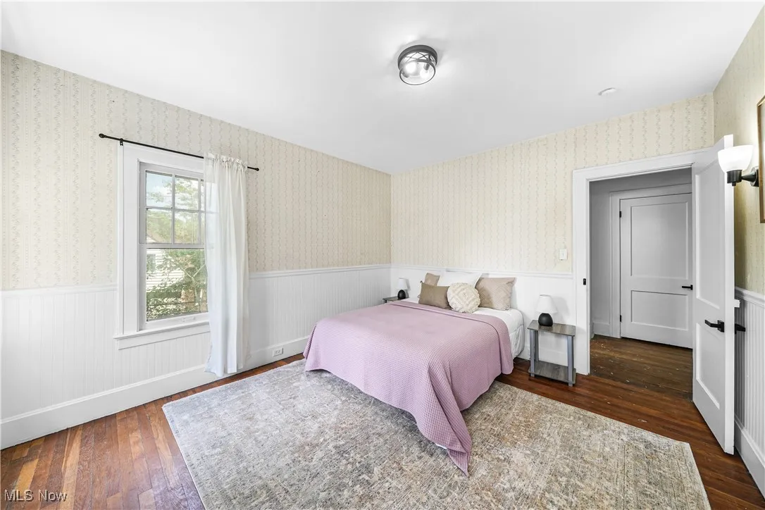 Bedroom with wallpapered walls, wainscoting, and wood-type flooring