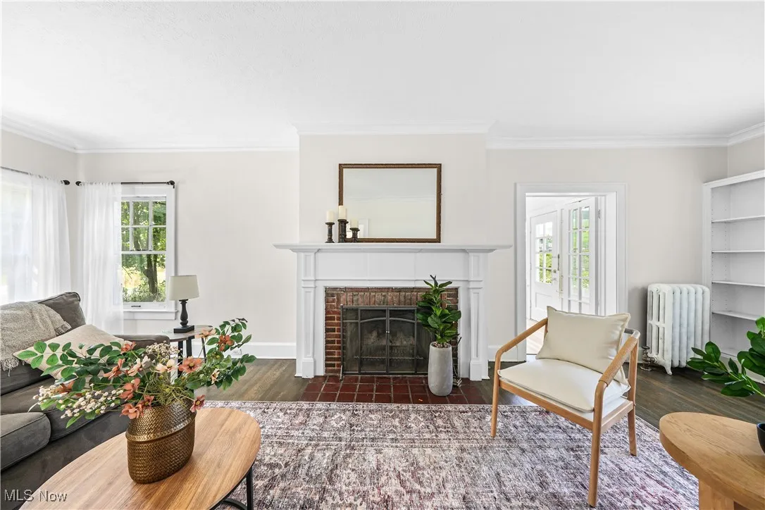 Living room featuring a brick fireplace, plenty of natural light, radiator, crown molding, and wood finished floors
