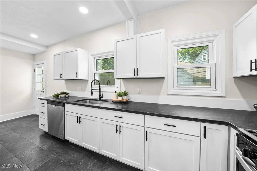 Kitchen with stainless steel dishwasher, white cabinets, dark countertops, recessed lighting, and stove