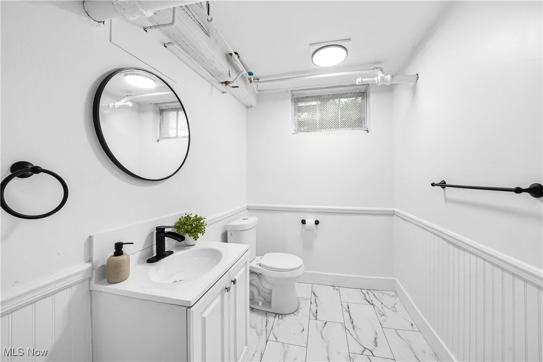 Bathroom featuring a wainscoted wall, marble look tile flooring, vanity, and a decorative wall