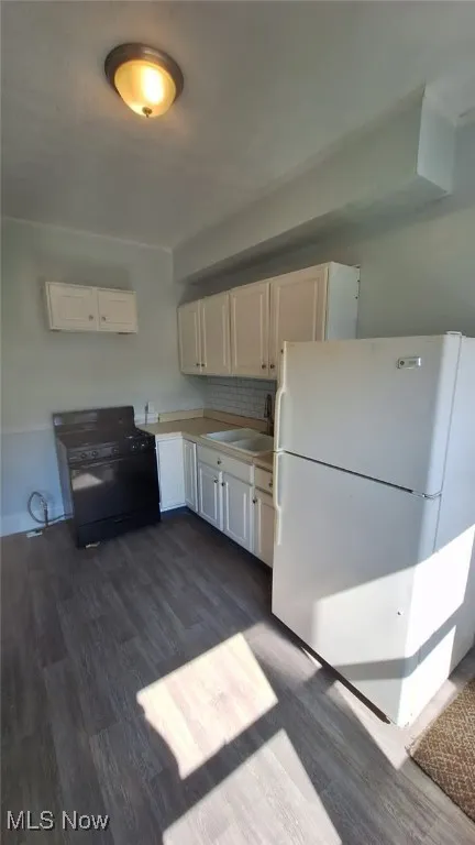 Kitchen with freestanding refrigerator, black gas stove, dark wood-style flooring, and white cabinets