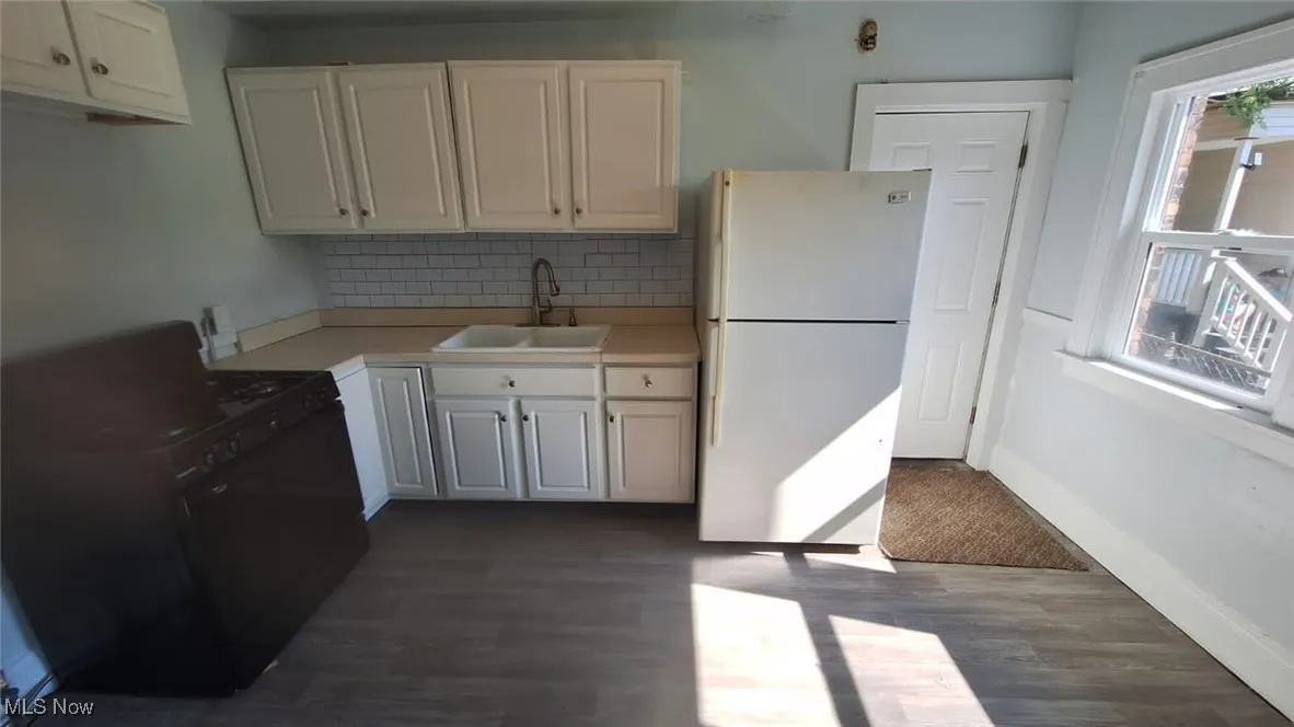 Kitchen with freestanding refrigerator, decorative backsplash, dark wood-type flooring, light countertops, and white cabinets