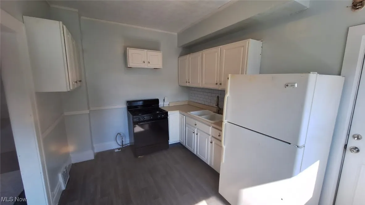 Kitchen with freestanding refrigerator, black gas range oven, dark wood finished floors, white cabinets, and light countertops