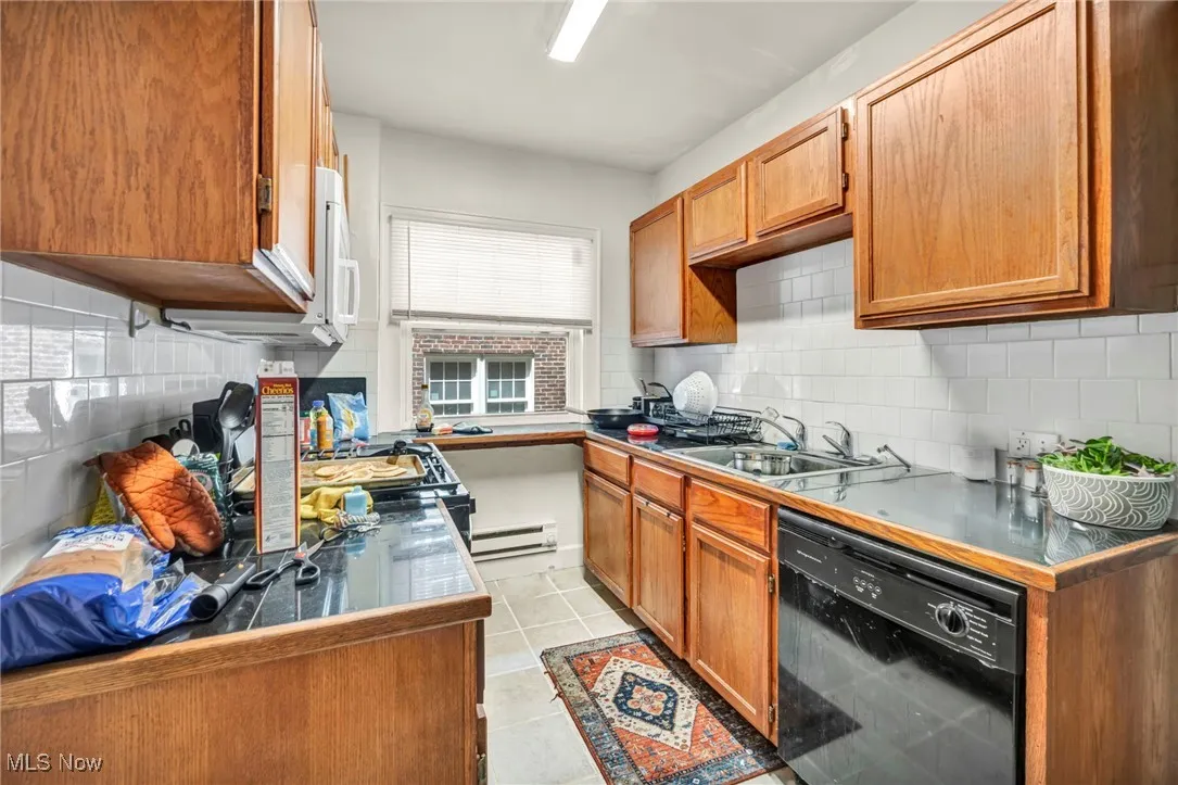 Kitchen with black dishwasher, brown cabinets, tasteful backsplash, and a baseboard radiator