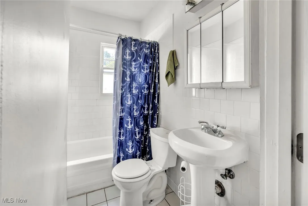 Full bath featuring tile walls, shower / bath combo with shower curtain, and tile patterned floors