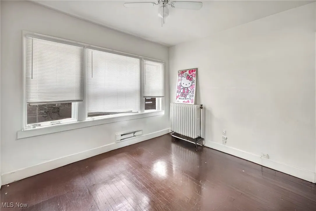 Empty room with wood-type flooring, radiator, a baseboard radiator, and a ceiling fan