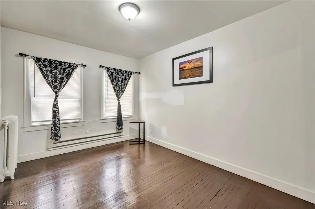 Unfurnished room with dark wood-style floors, a baseboard radiator, and radiator heating unit