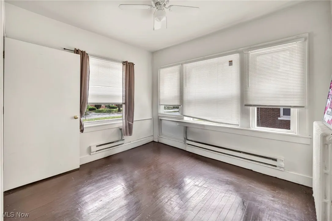 Empty room featuring dark wood finished floors, radiator heating unit, and ceiling fan