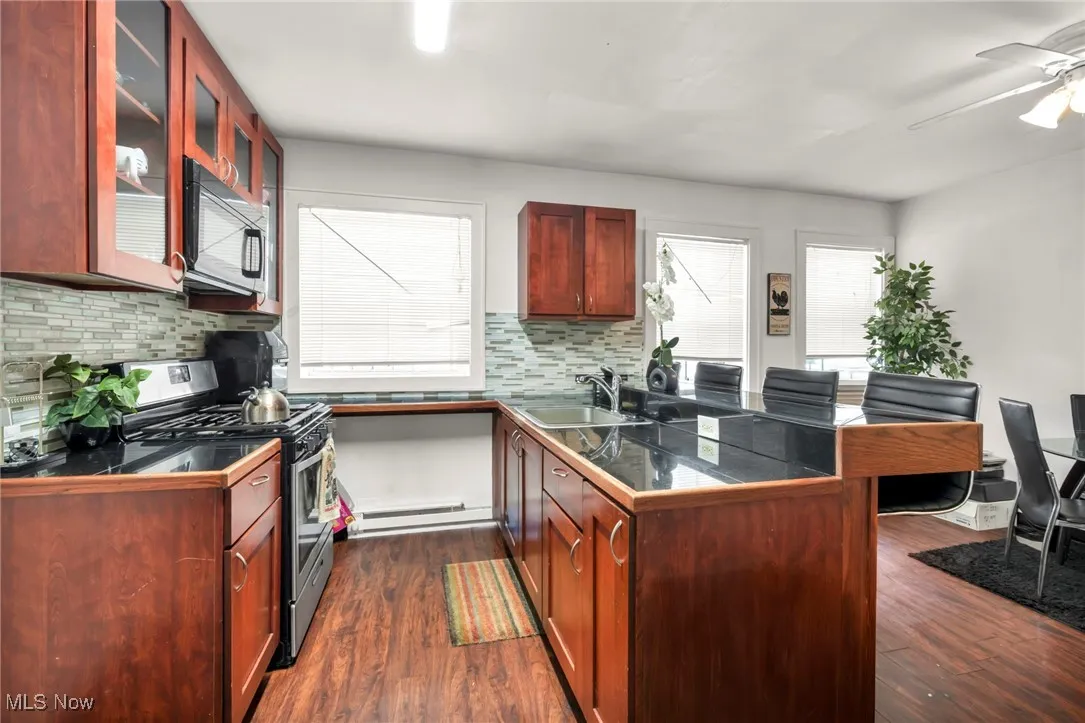 Kitchen featuring a peninsula, stainless steel gas range oven, dark wood finished floors, black microwave, and glass insert cabinets