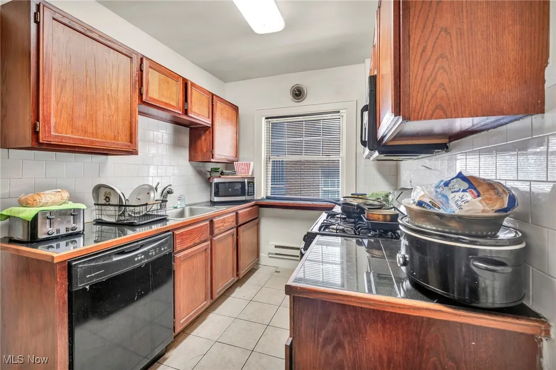 Kitchen with dishwasher, light tile patterned floors, brown cabinetry, tasteful backsplash, and stainless steel microwave