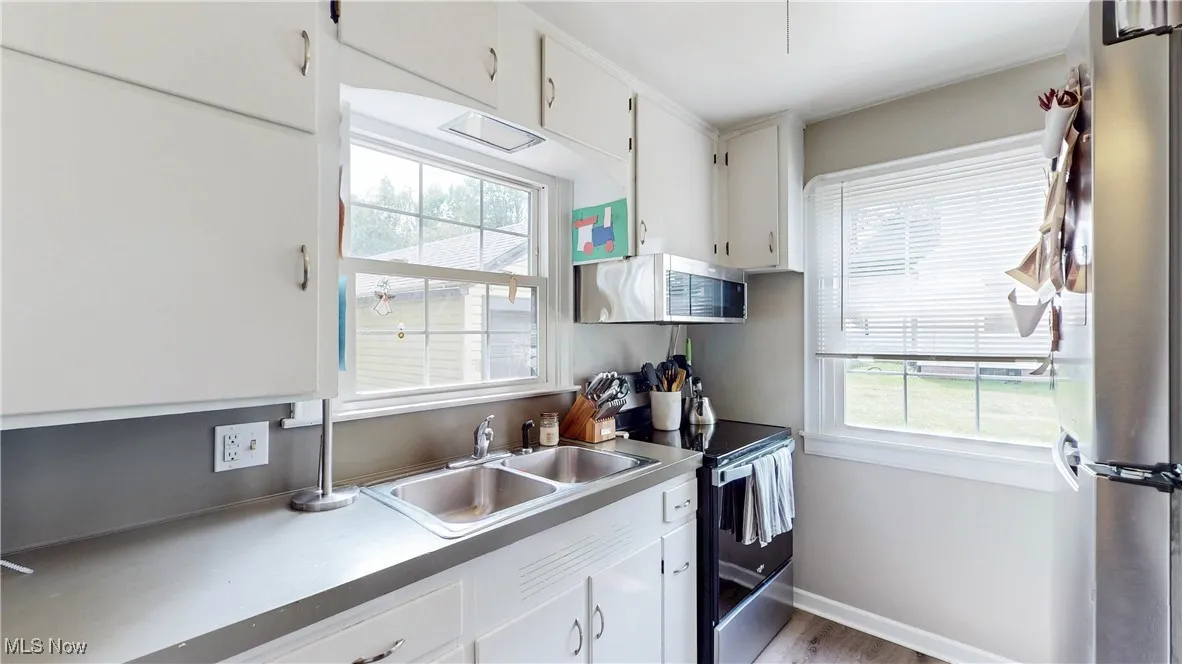 Kitchen with stainless steel appliances, healthy amount of natural light, white cabinets, and wood finished floors