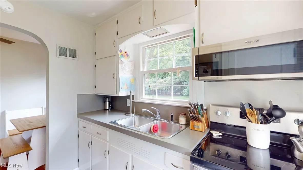 Kitchen featuring stainless steel appliances, light countertops, white cabinets, and arched walkways