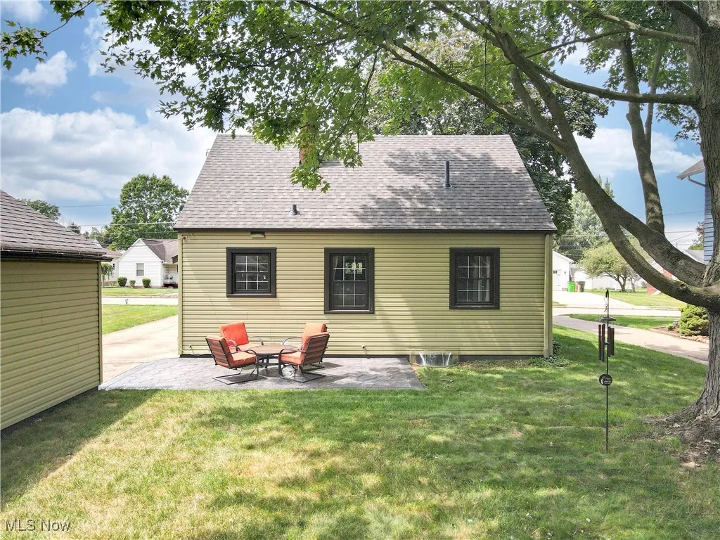Rear view of house featuring a patio, a lawn, and a shingled roof