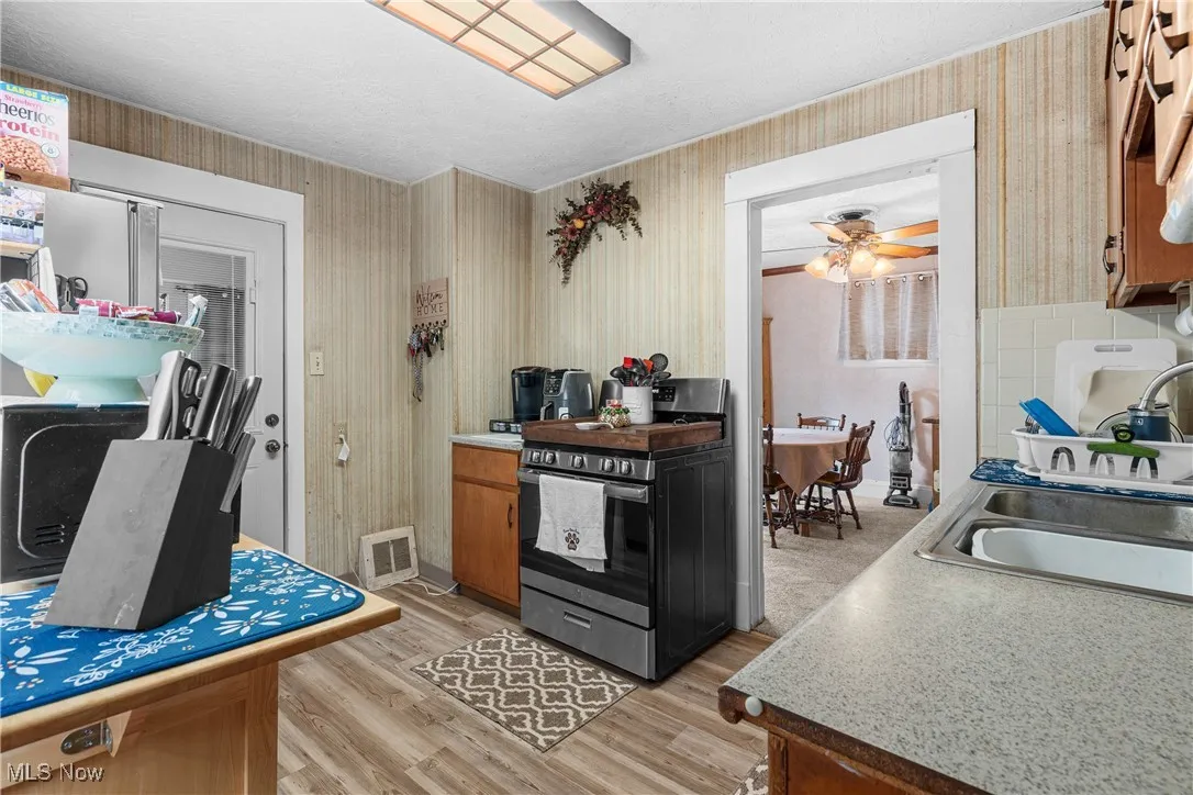 Kitchen with stainless steel range with gas cooktop, wallpapered walls, light wood-type flooring, light countertops, and brown cabinetry