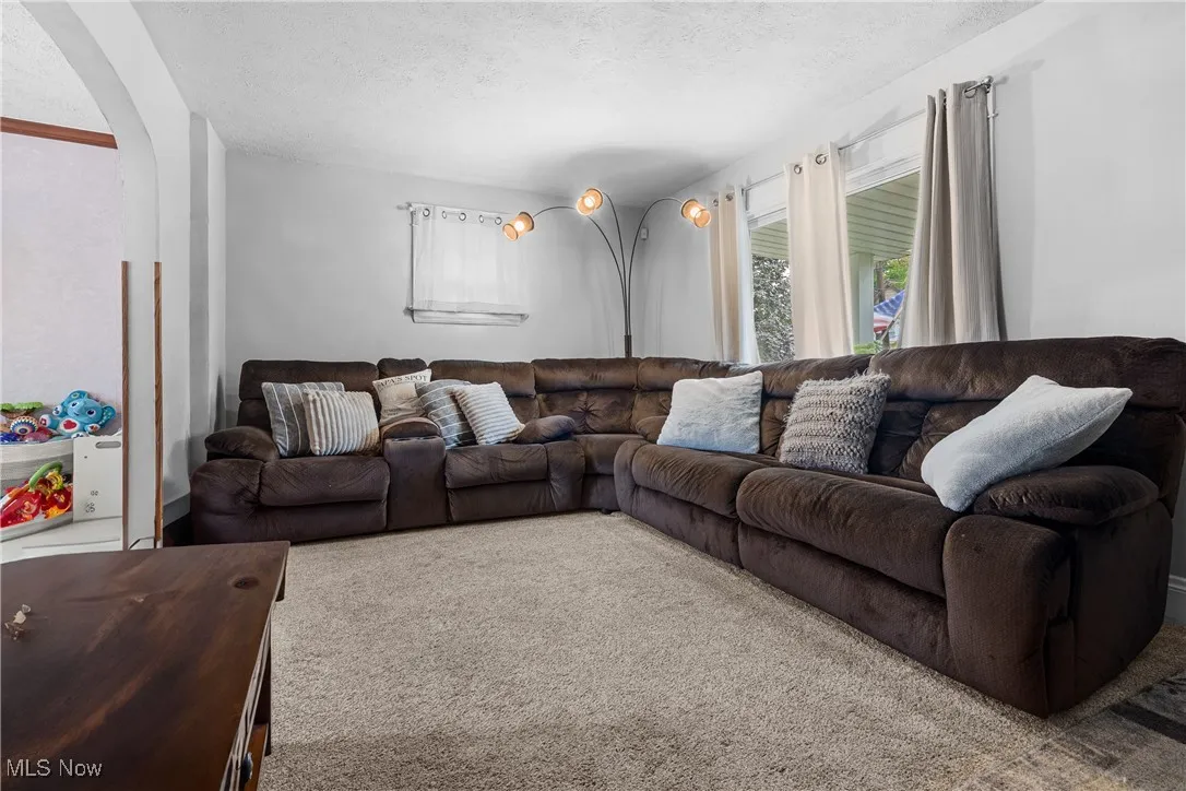Carpeted living room with arched walkways, a textured ceiling, and plenty of natural light