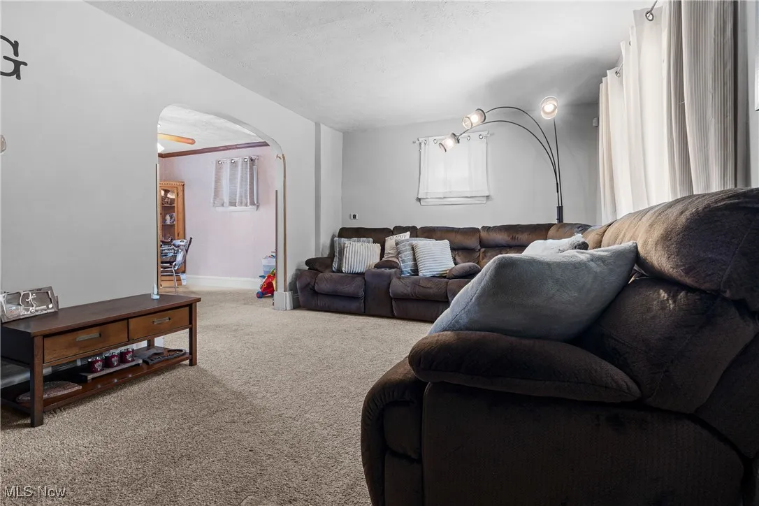 Living area featuring carpet floors, arched walkways, a textured ceiling, and crown molding