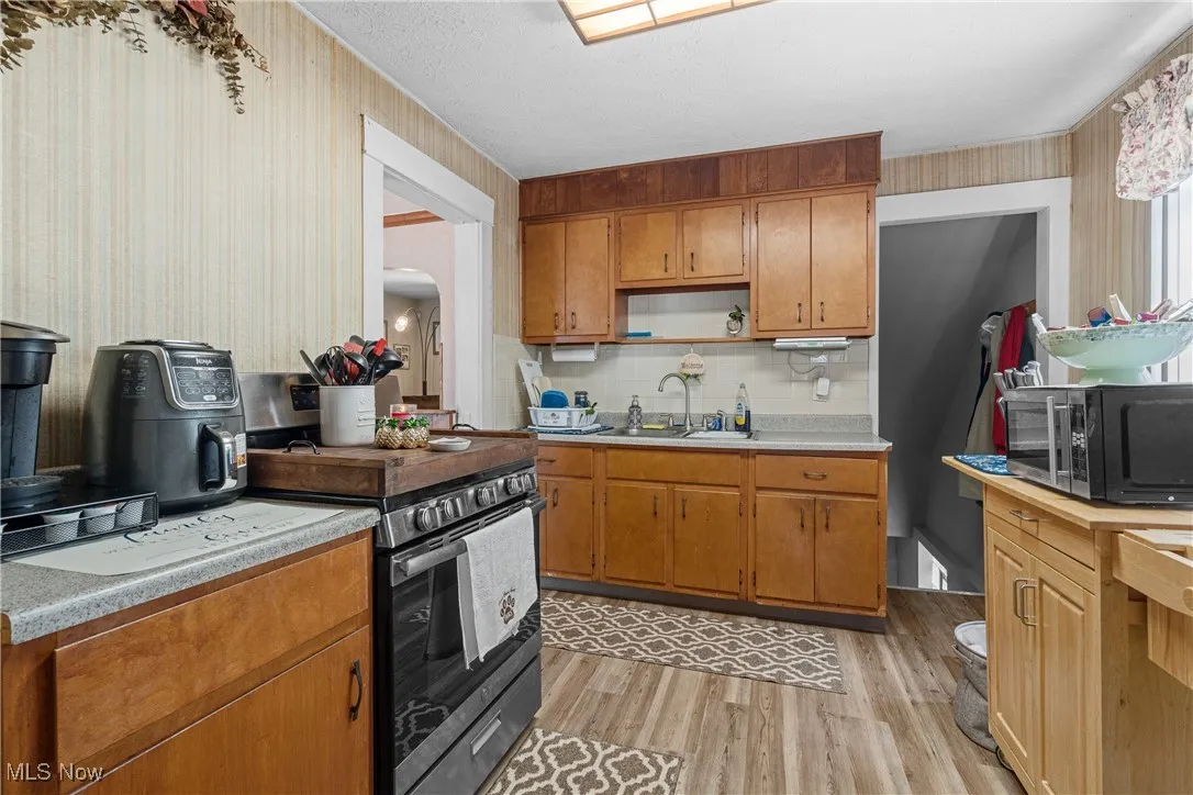 Kitchen featuring wallpapered walls, light wood-style flooring, light countertops, stainless steel electric stove, and open shelves