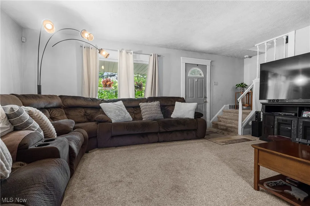 Living room featuring carpet flooring, a textured ceiling, and stairway