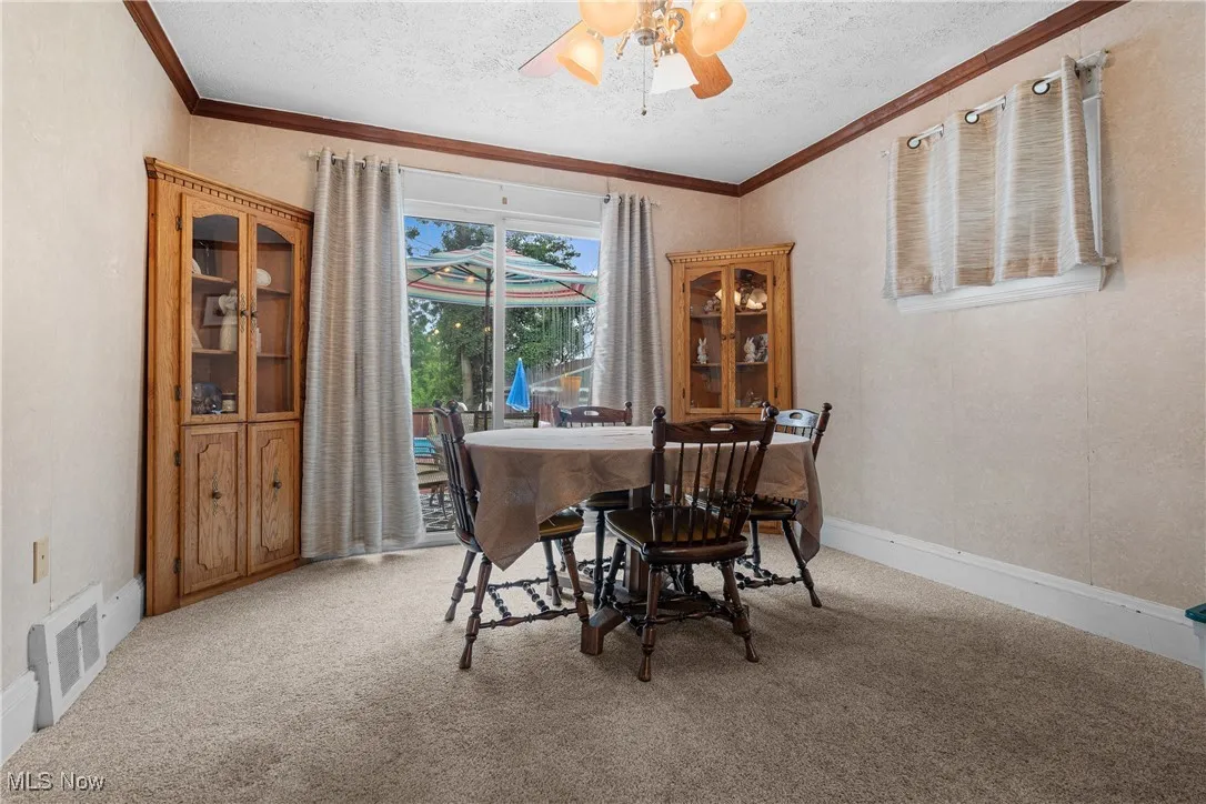 Dining room with light colored carpet, ornamental molding, a ceiling fan, and a textured ceiling