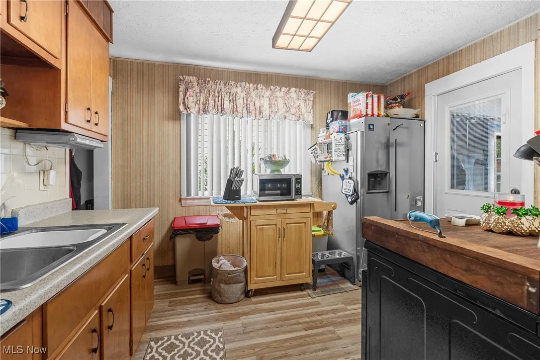 Kitchen featuring stainless steel appliances, light countertops, light wood finished floors, wallpapered walls, and a textured ceiling