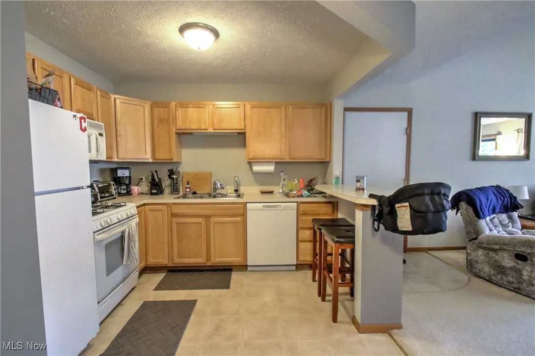 Kitchen with white appliances, light brown cabinets, light countertops, a textured ceiling, and a peninsula
