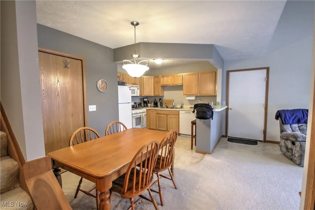 Dining space with a textured ceiling, light carpet, lofted ceiling, and stairway