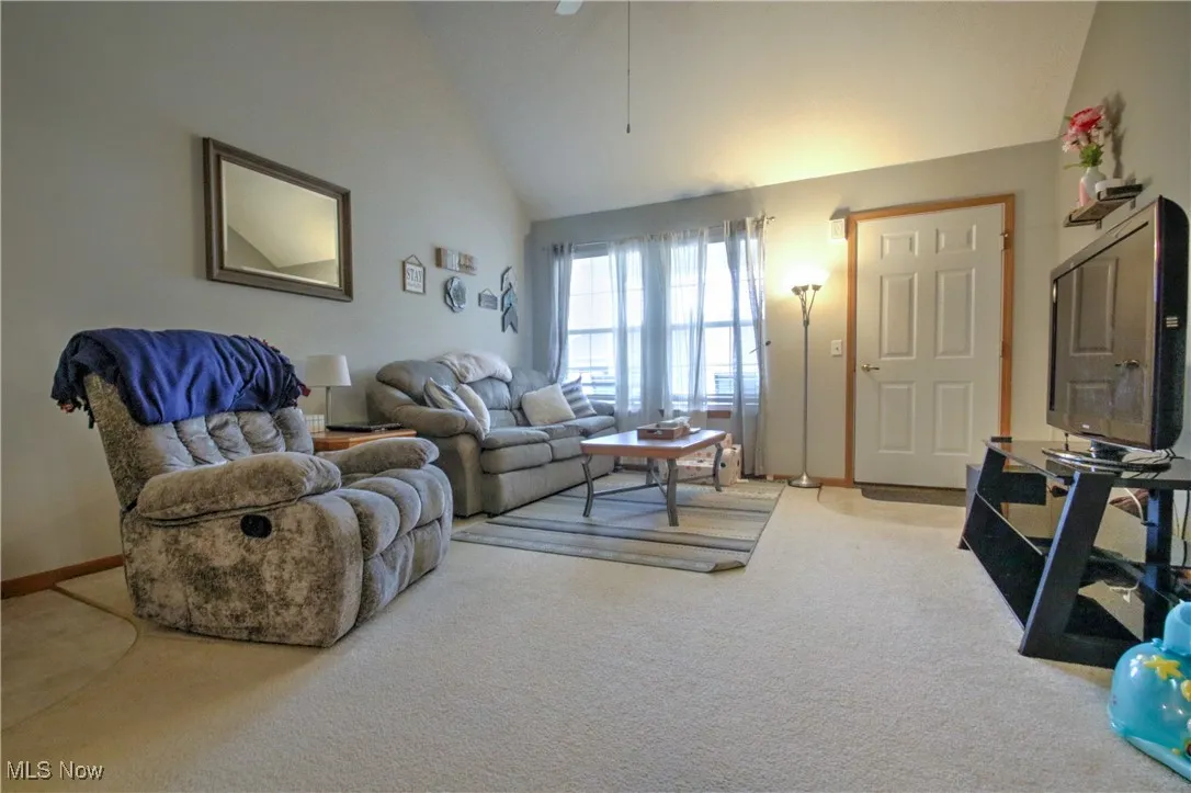 Living room with carpet flooring, high vaulted ceiling, and a ceiling fan