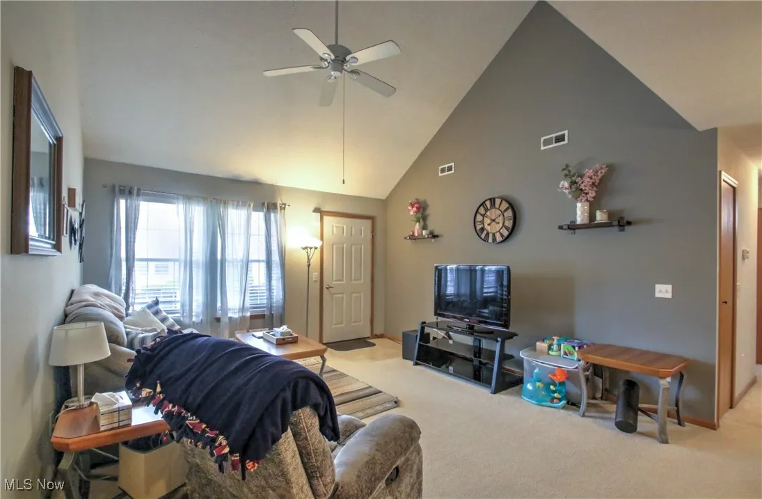Carpeted living area with high vaulted ceiling and a ceiling fan