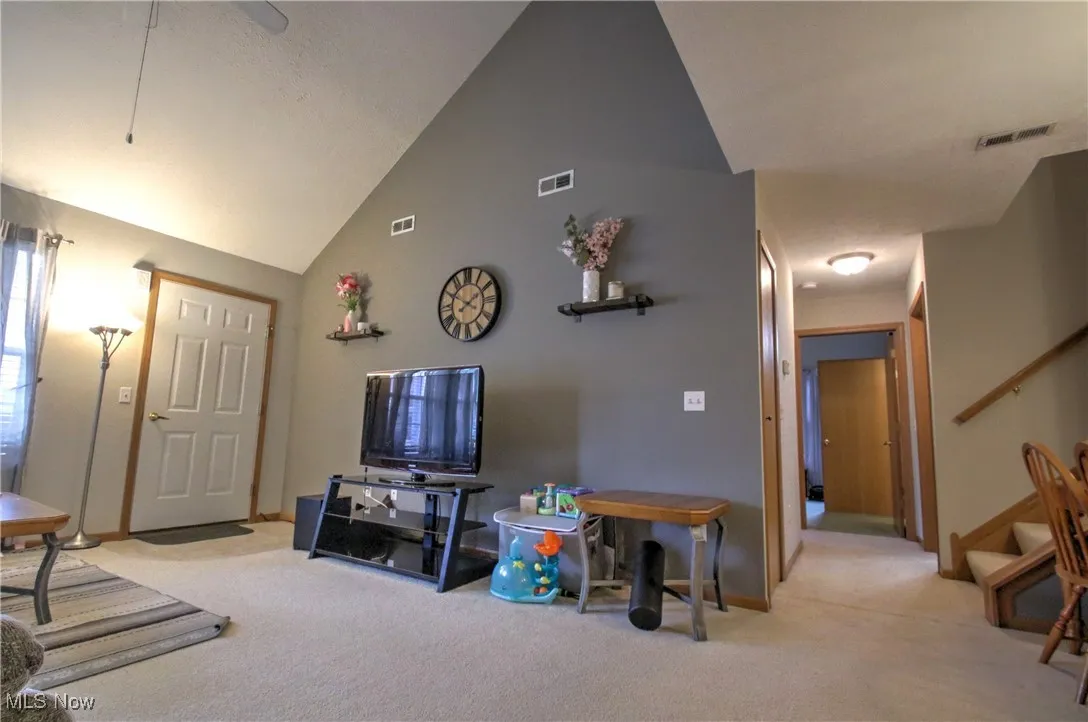 Carpeted living area featuring high vaulted ceiling, stairway, and ceiling fan