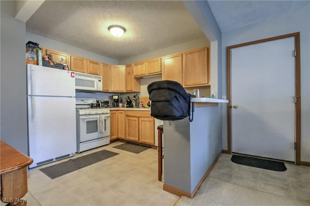 Kitchen featuring a textured ceiling, white appliances, light brown cabinets, light flooring, and light countertops
