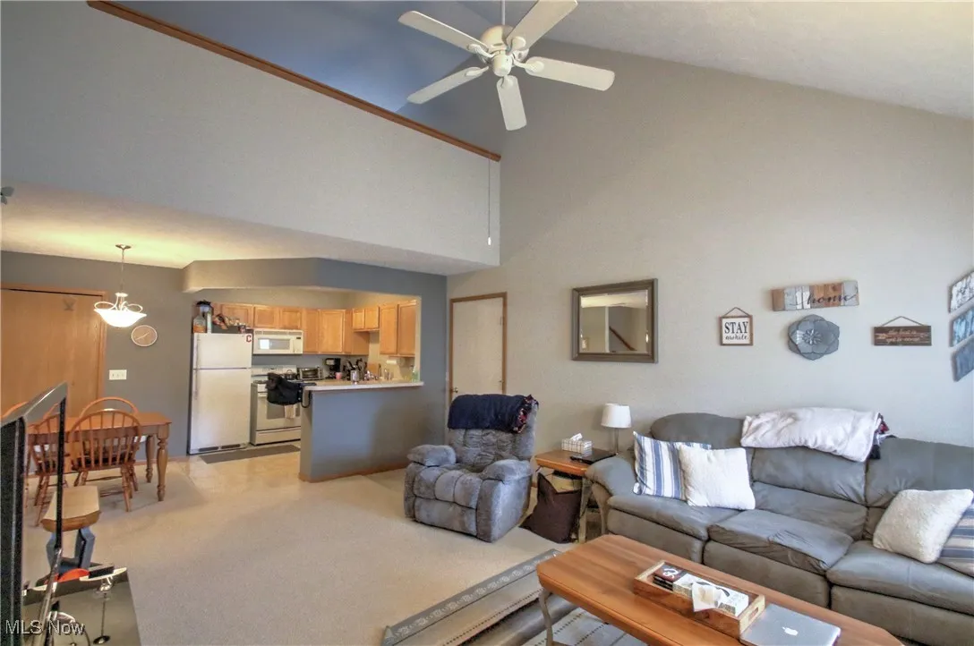 Living area with high vaulted ceiling, ceiling fan, and light colored carpet