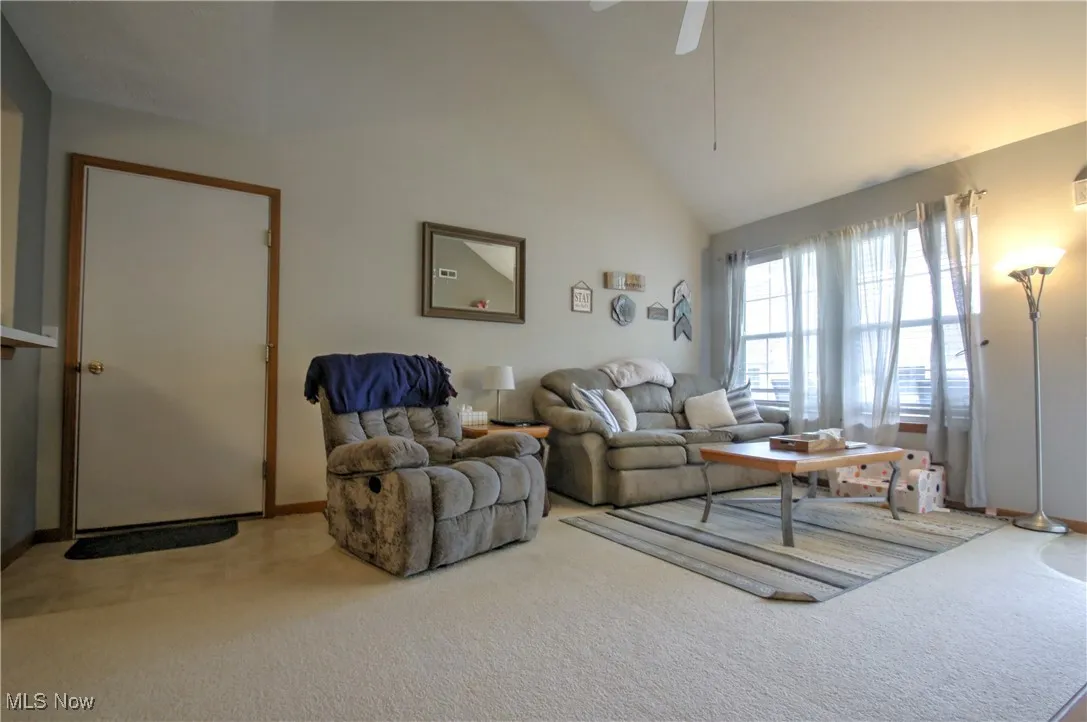 Living area featuring high vaulted ceiling, carpet flooring, and a ceiling fan