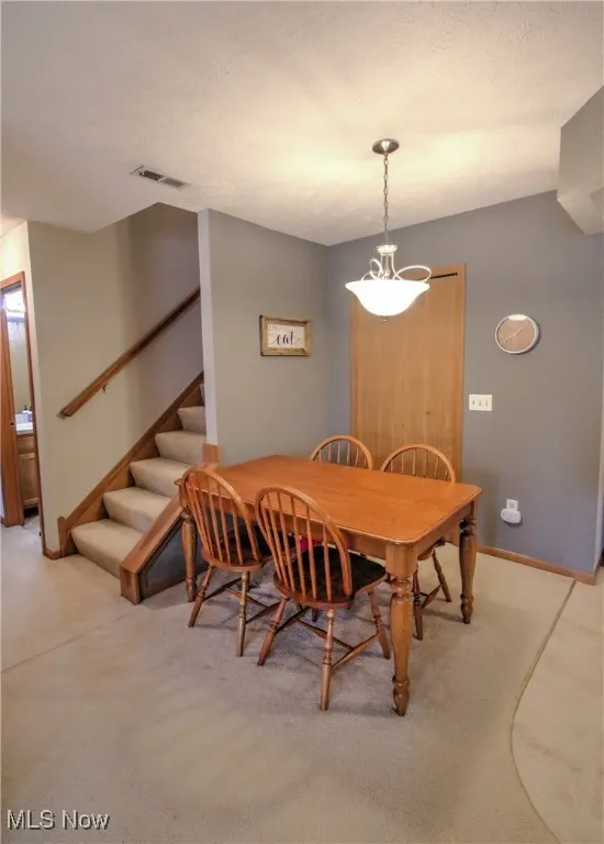 Carpeted dining room with stairs and baseboards