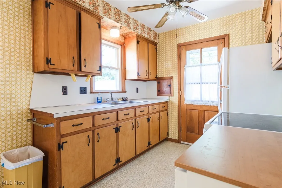 Kitchen with wallpapered walls, freestanding refrigerator, light countertops, a ceiling fan, and range