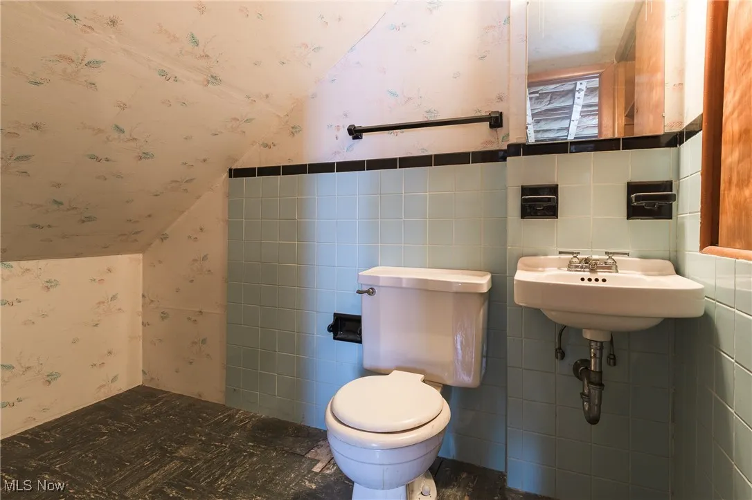 Bathroom featuring wallpapered walls and vaulted ceiling