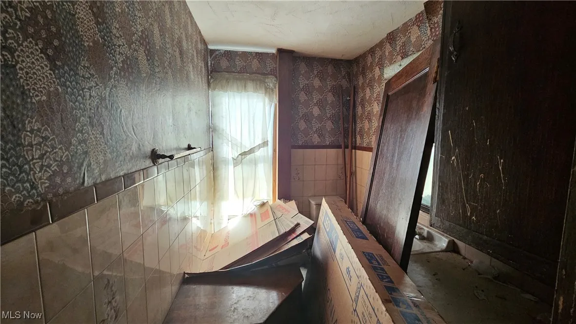 Bathroom featuring tile walls, wallpapered walls, and a wainscoted wall