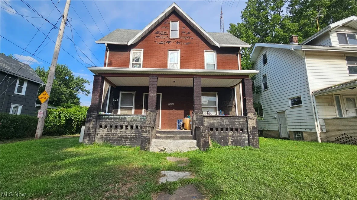 View of front facade featuring covered porch, a front lawn, and brick siding