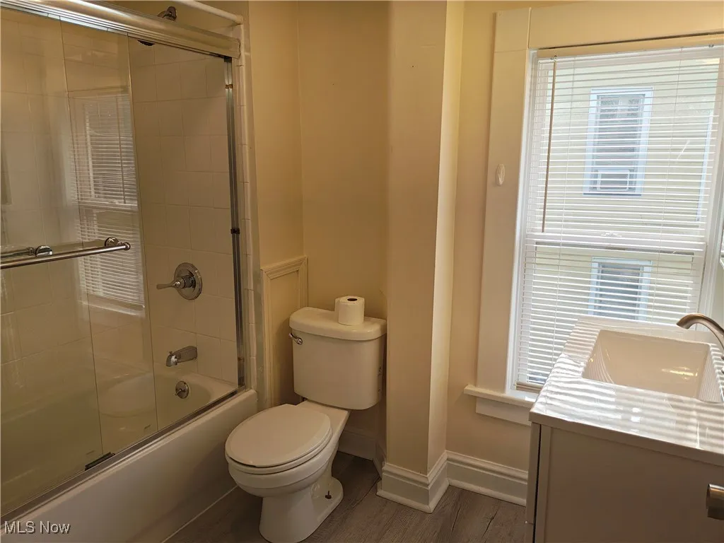 Bathroom with bath / shower combo with glass door, wood finished floors, and vanity
